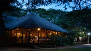 A thatched-roof building with a covered outdoor area, stairs leading to the entrance, and a well-maintained garden. - Falaza Game Lodge (Hluhluwe)