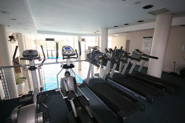 A gym with treadmills, elliptical machines, and a pool area visible through the windows. - Knightsbridge 902E by CTHA (Cape Town)