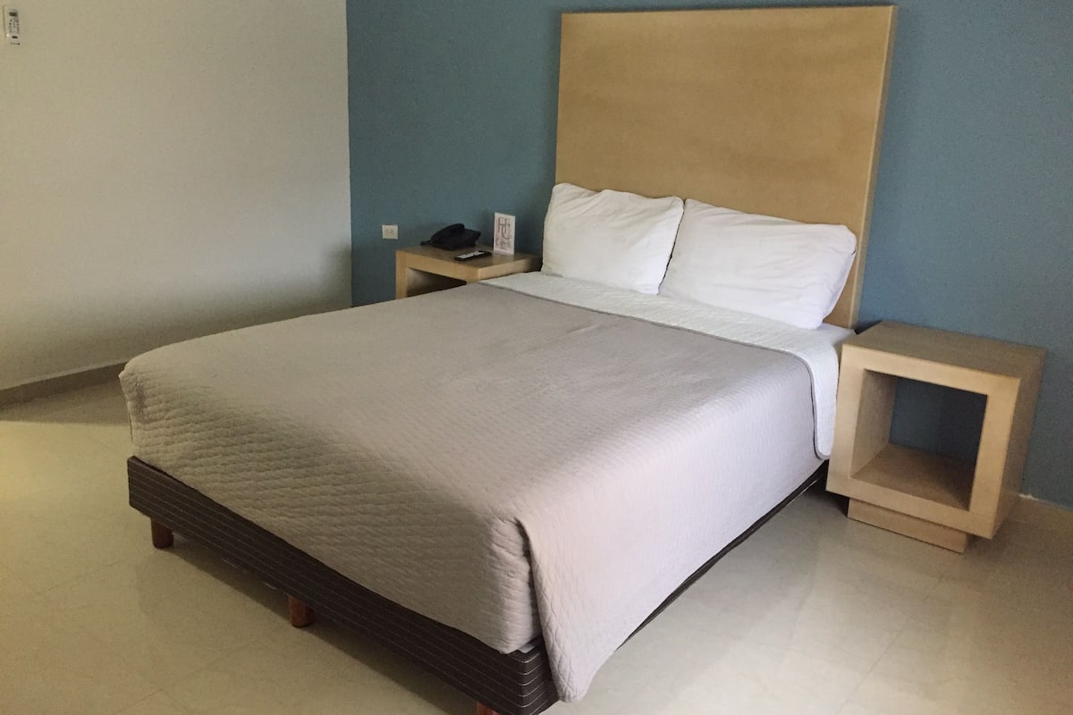 A neatly made bed with a wooden headboard, a bedside table with a lamp, and a small nightstand with a phone.