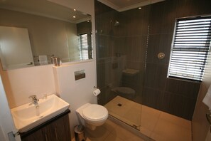 Un baño moderno con lavamanos, inodoro y ducha con mampara de vidrio.