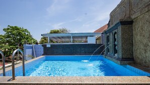 A swimming pool with a clear blue water, a covered area, and a stone wall. - Reddoorz @ Cemara Beach Sunrise (Denpasar)