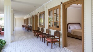 A corridor with wooden chairs and tables, a bed, and a white brick wall. - Reddoorz @ Cemara Beach Sunrise (Denpasar)