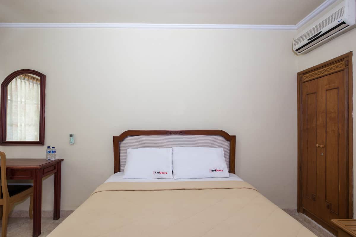 Ein Hotelzimmer mit Bett, Schreibtisch aus Holz, Stuhl, Kleiderschrank und Klimaanlage.