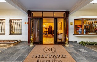 The entrance to Sheppard Boutique Hotel with a doormat, a reception desk, and a view of the interior through the glass doors.