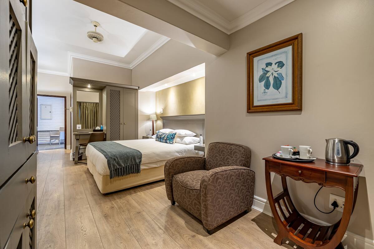 Une chambre d’hôtel avec un lit, une chaise, une petite table avec une bouilloire et un tableau encadré au mur.