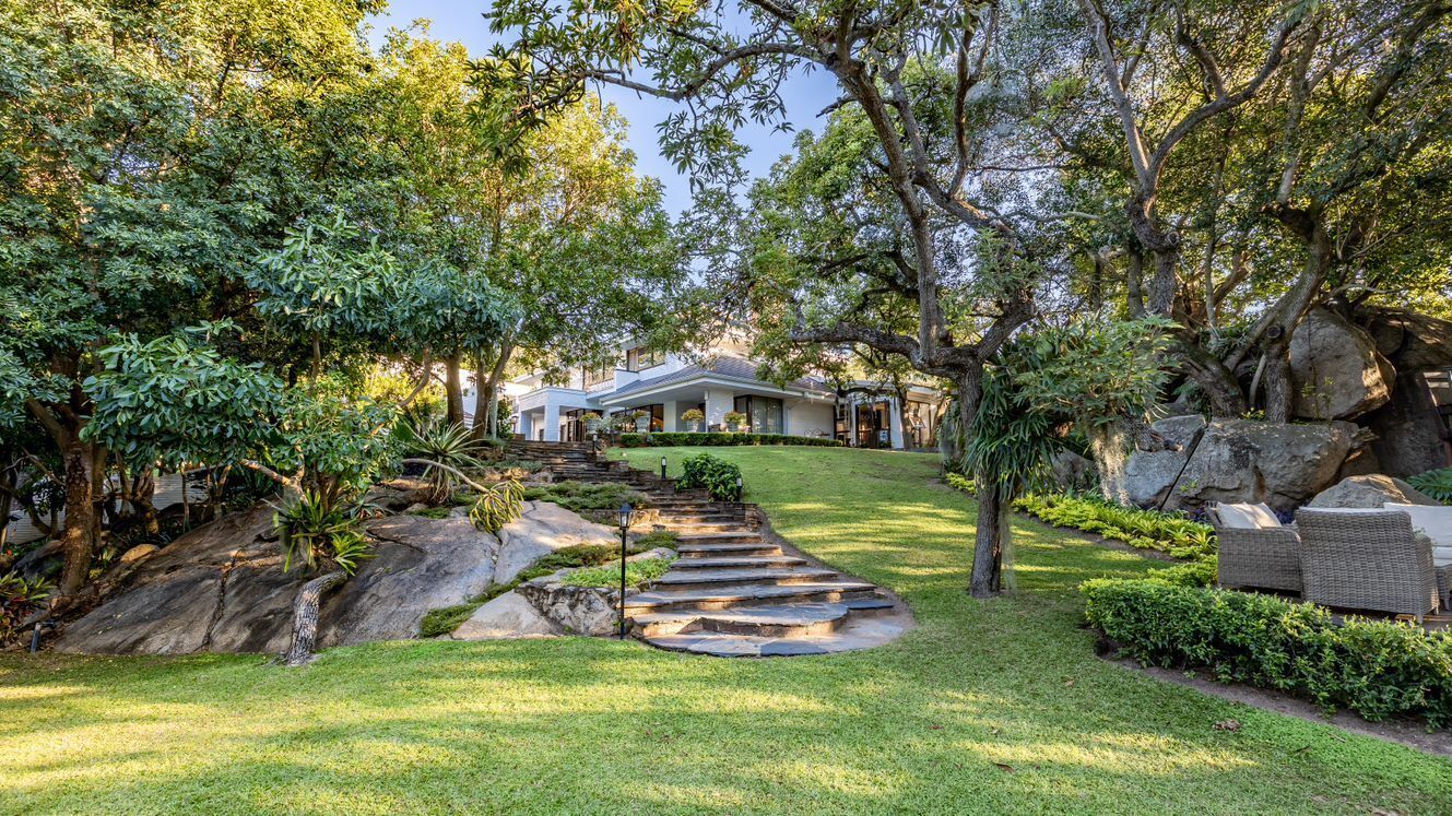 A house with a stone pathway leading to the front door, surrounded by lush greenery and trees.