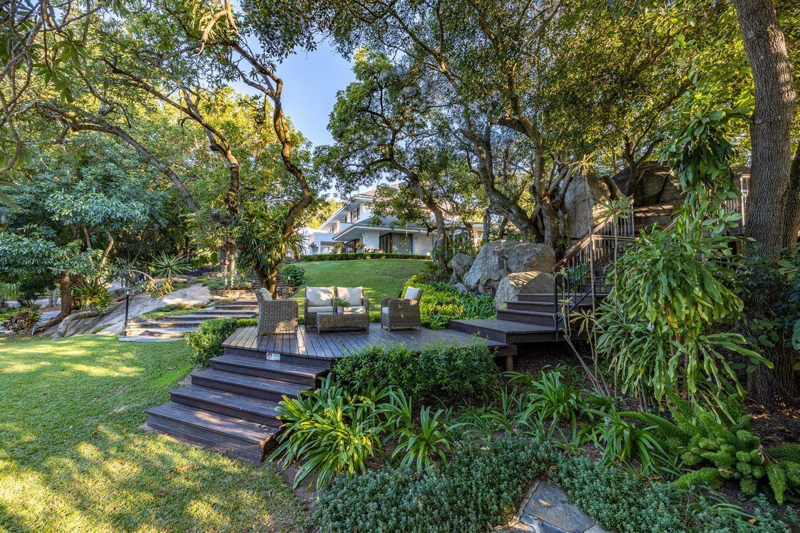 A well-maintained garden with a wooden deck, outdoor furniture, and a variety of plants.