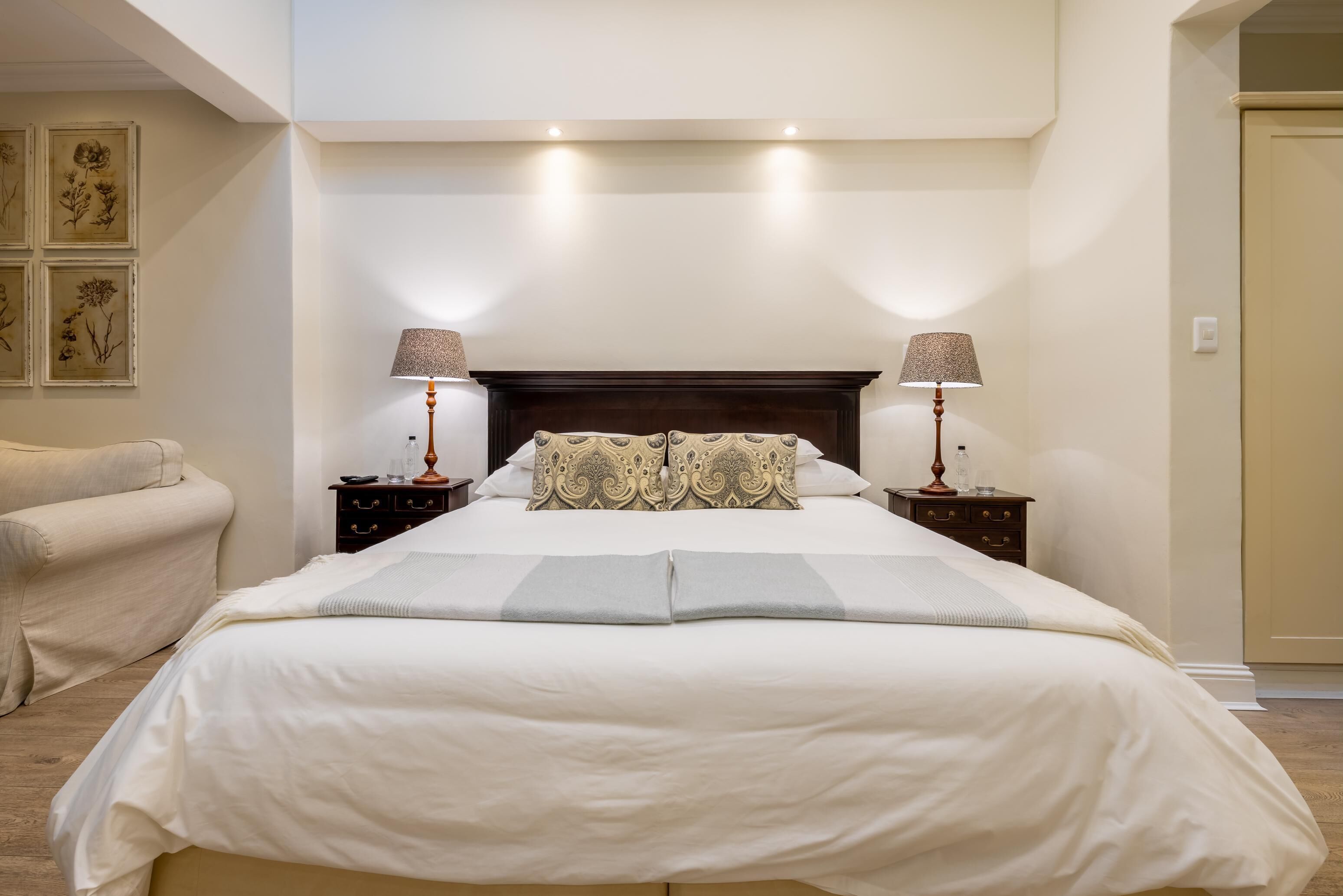 Una cama bien hecha con cabecera, dos mesitas de noche con lámparas y una silla.