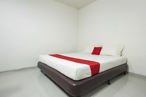 A neatly made bed with a white mattress and a red accent, a dark headboard, and a white wall.