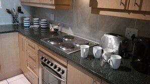 A modern kitchen with stainless steel appliances, wooden cabinets, and a granite countertop. - Bougain Villas Apartments (Cape Town)