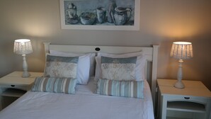 A neatly made bed with floral pillows, two bedside lamps, and a framed painting above. - Bougain Villas Apartments (Cape Town)