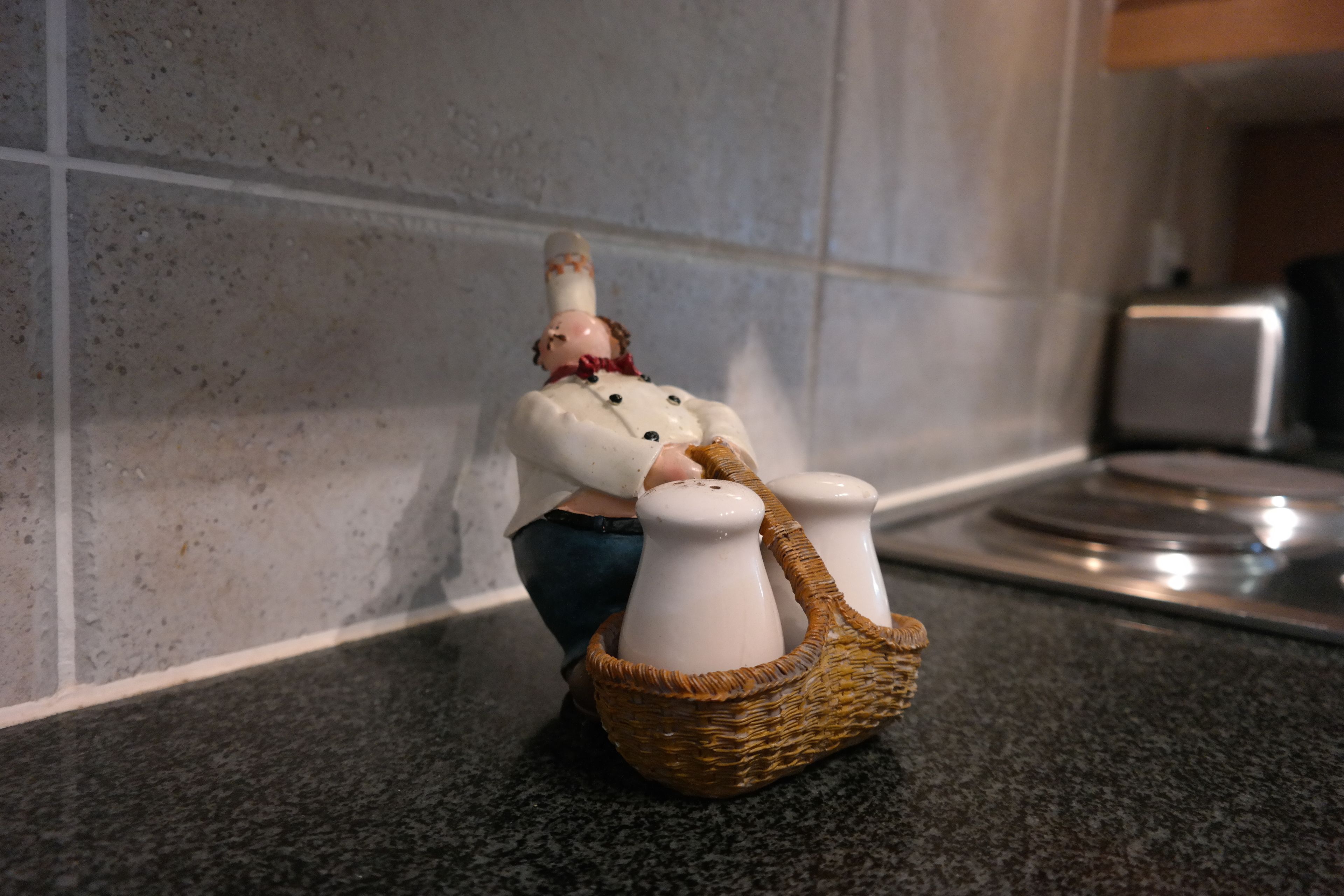 A kitchen counter with a ceramic figurine of a person in a white shirt and blue pants, holding a basket with two white pitchers.