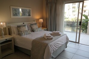 Una camera d'albergo con un letto grande, due comodini con lampade e vista sul balcone, oltre a un quadro appeso al muro.