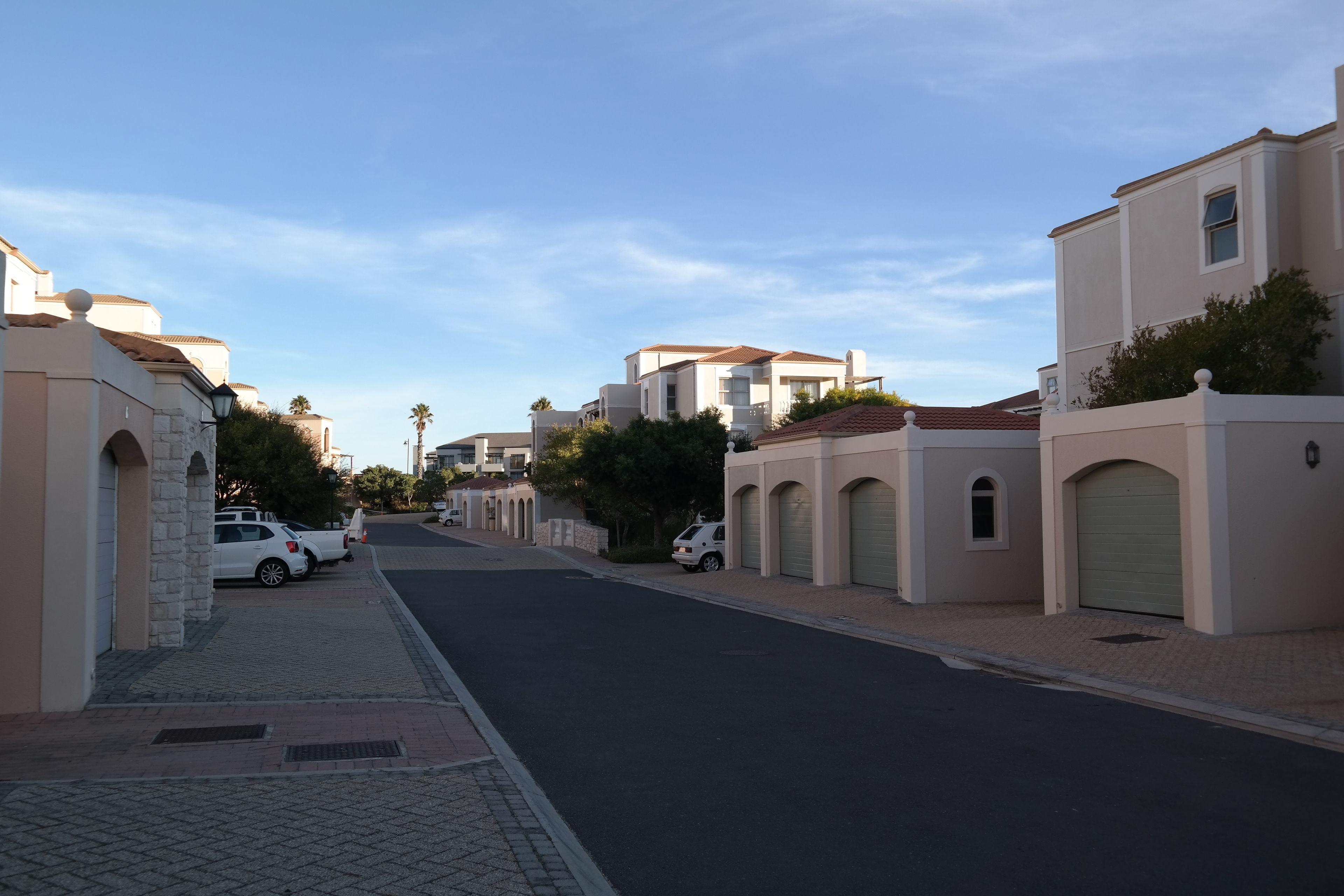 A residential street with modern houses, paved sidewalks, and parked cars.