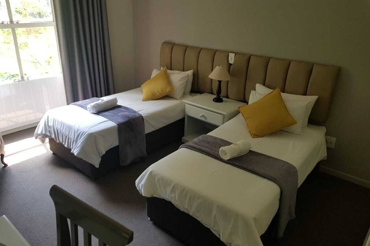 Une chambre d’hôtel avec deux lits simples, une table de chevet, une lampe et une chaise.
