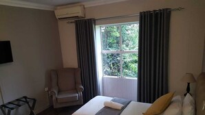 Una camera d'albergo con un letto, una sedia, una scrivania e una finestra con tende.