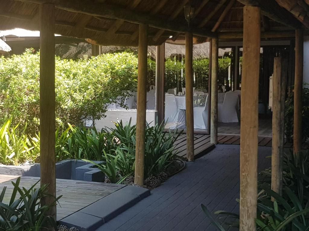 A covered outdoor area with wooden columns, tables with white tablecloths, and lush greenery.