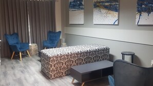 Una camera d'albergo compatta con un letto, due poltrone blu, un tavolino e una scrivania con dispenser d'acqua.