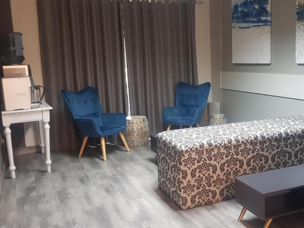 A room with a bed, two blue chairs, a small table, and a curtain.