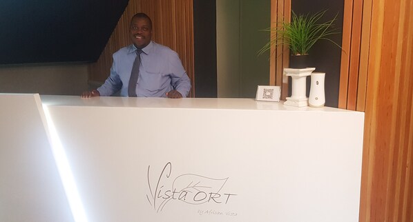 A reception desk with a logo, a potted plant, and a framed item on the counter. - Vista ORT (Kempton Park)