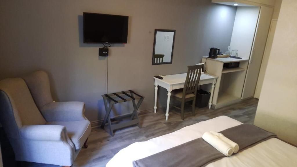 Una habitación de hotel con una cama, un escritorio, una silla, un televisor y un espejo.