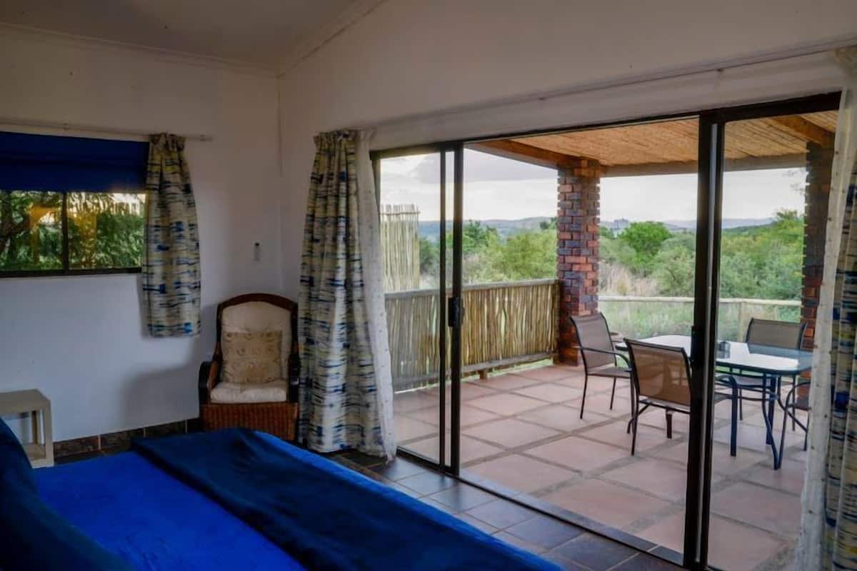 A bedroom with a bed, a chair, and a balcony with a table and chairs.