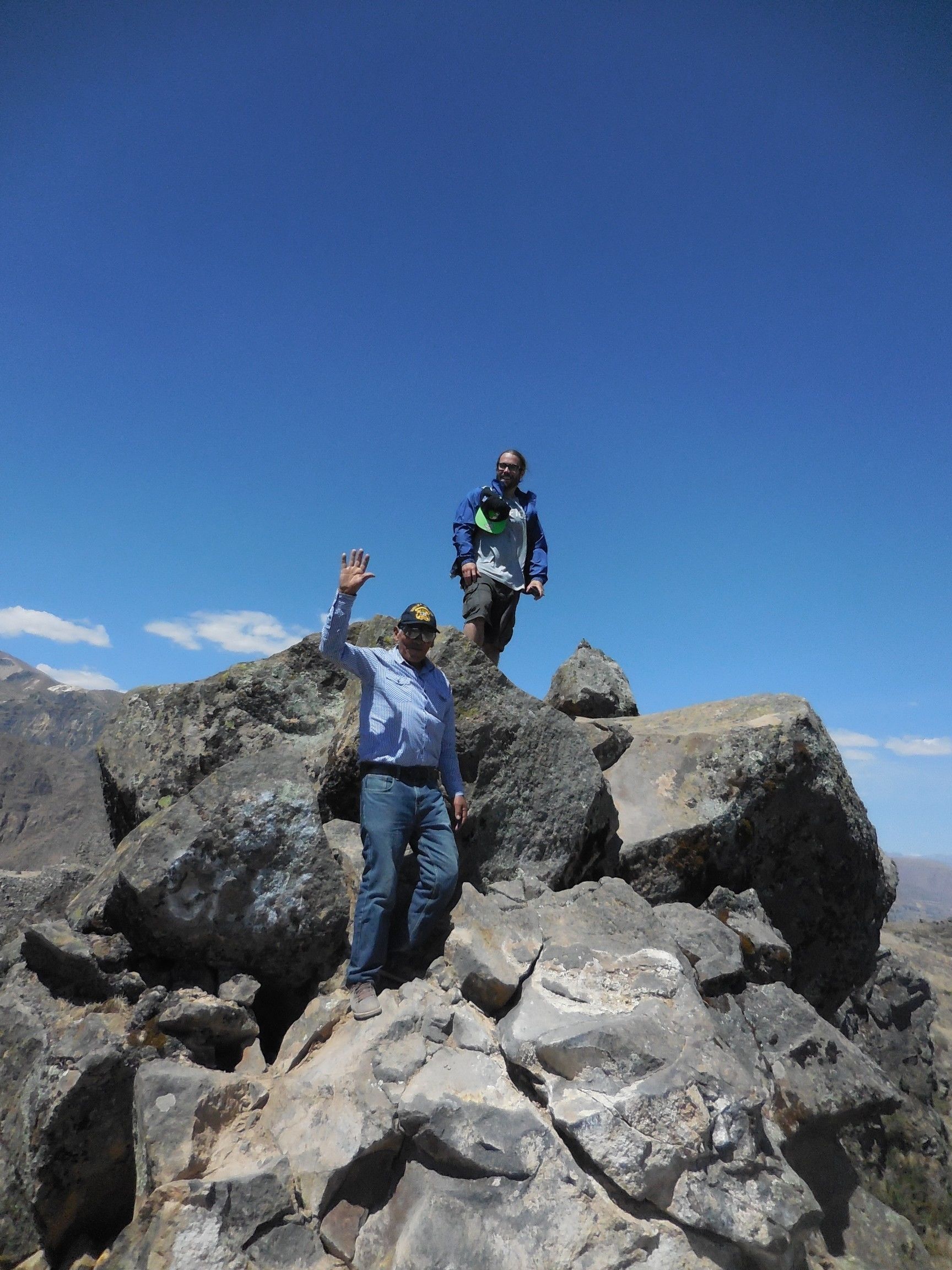 Two people standing on rocky terrain with a clear blue sky in the background.
