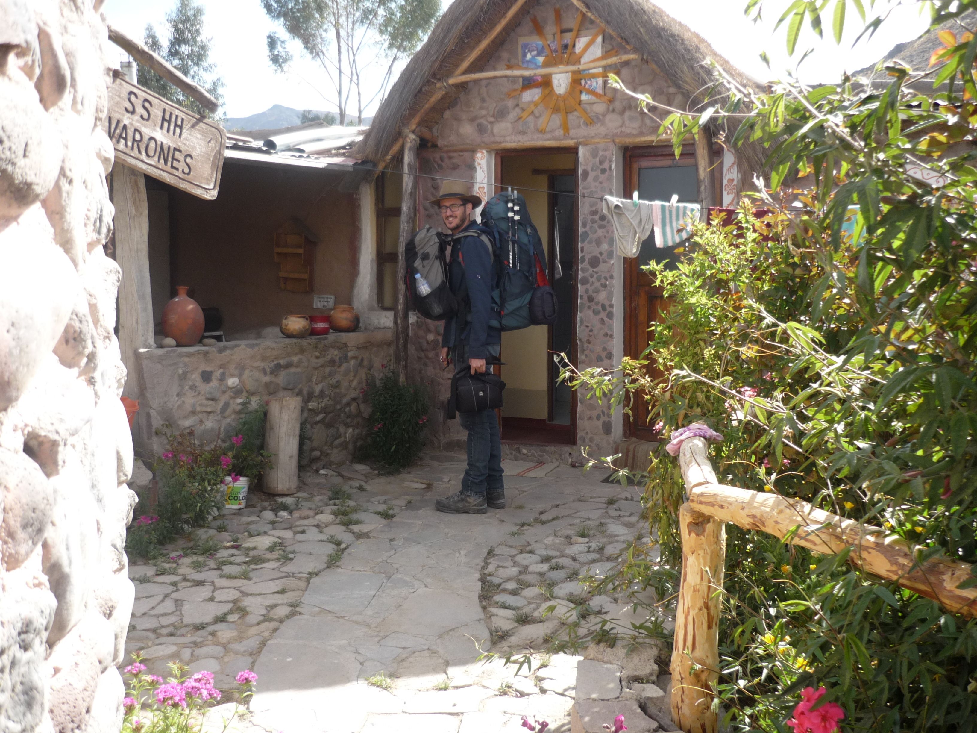 A stone building with a thatched roof, a sign reading "SS HH VARONES", and a person standing in front.