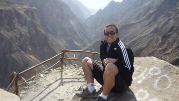 A person sitting on a stone ledge with a mountainous landscape in the background.