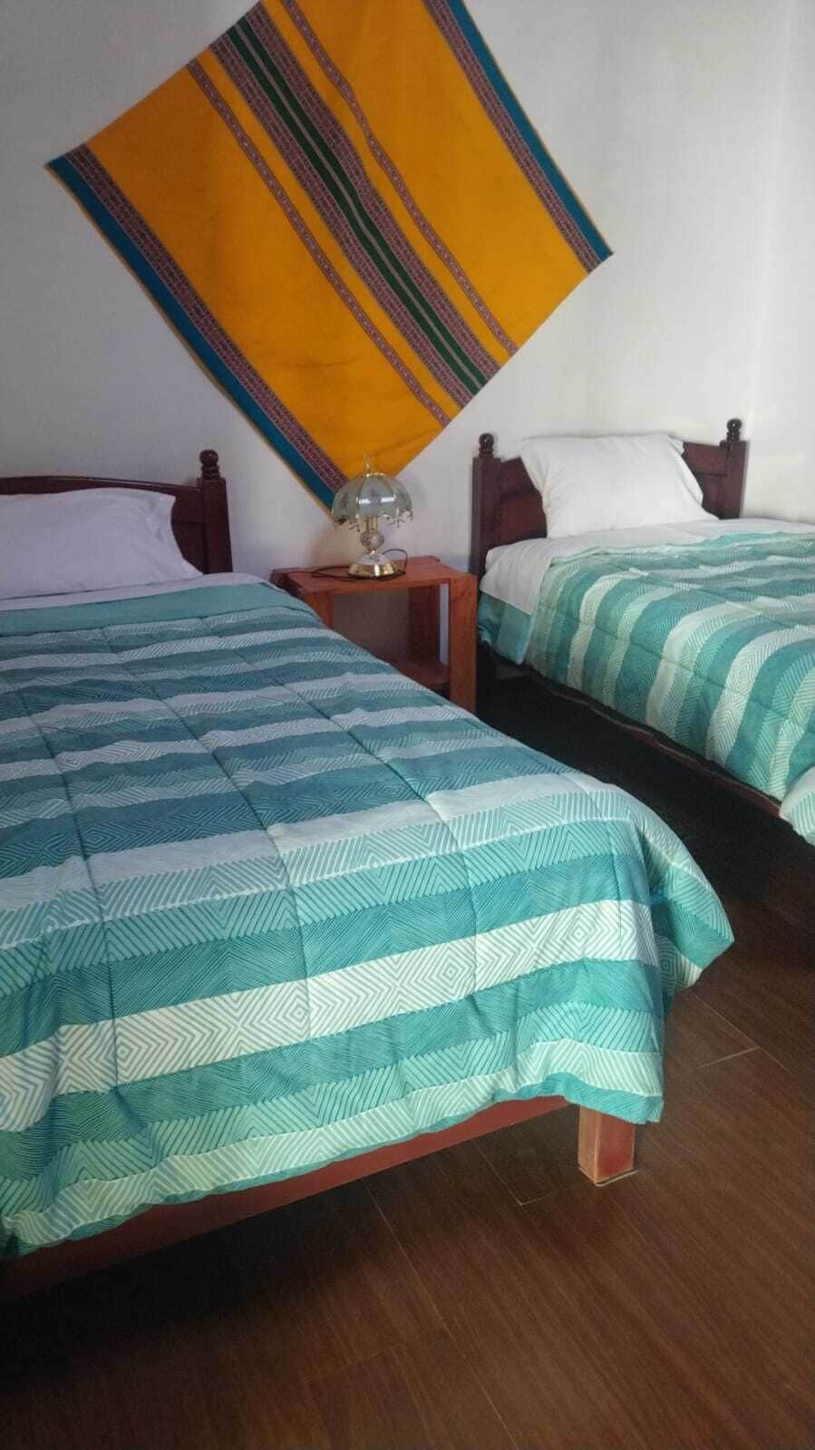 Two beds with striped bedding, a nightstand with a lamp, and a hanging tapestry.