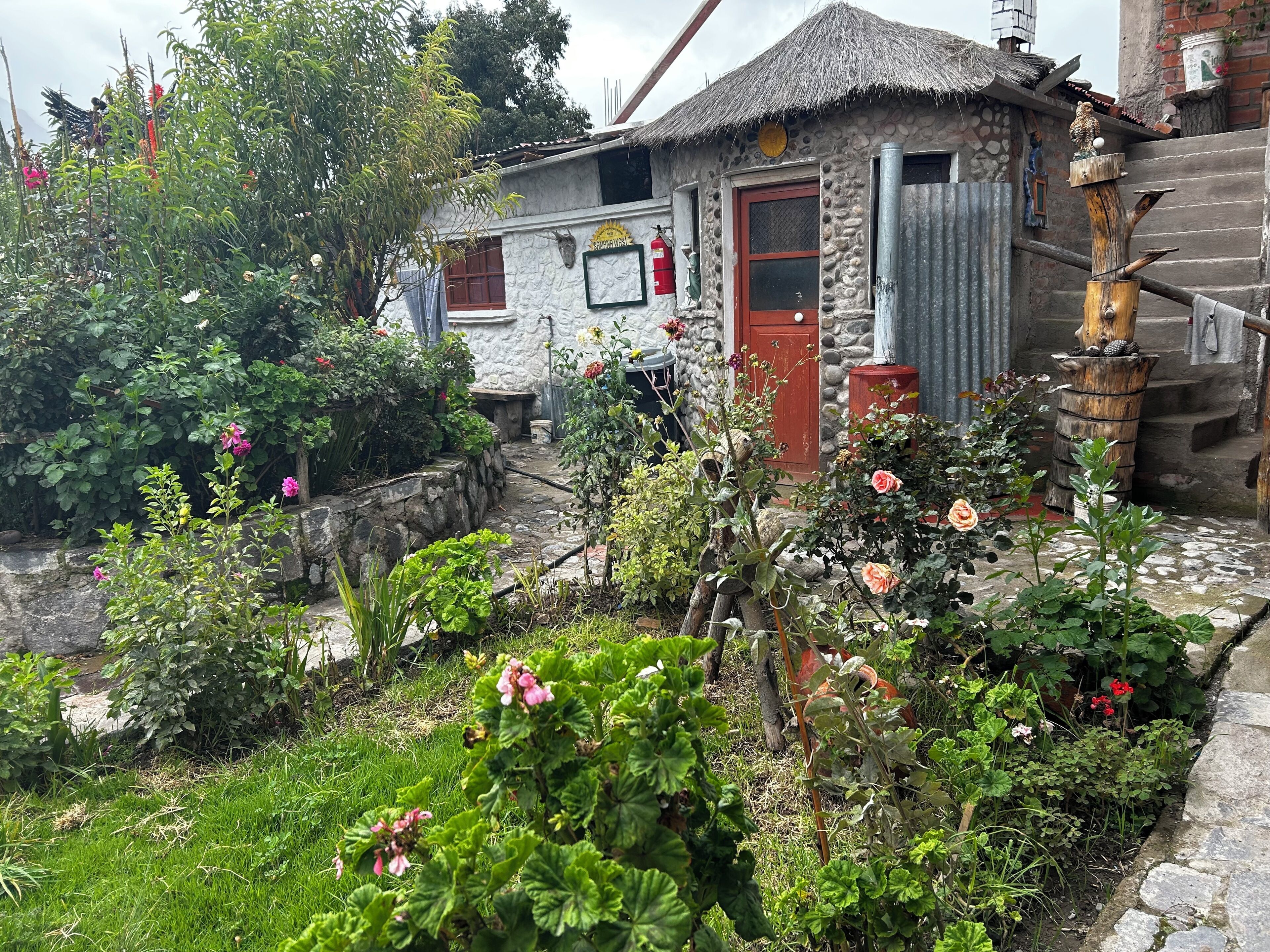 A rustic stone building with a thatched roof, surrounded by a garden with various plants and flowers.