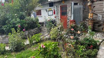 Un edificio rústico de piedra con techo de paja, rodeado de un jardín con diversas plantas y flores.
