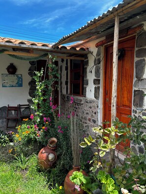 A rustic stone building with a wooden door, a window, and a small porch area with a chair and a poster.