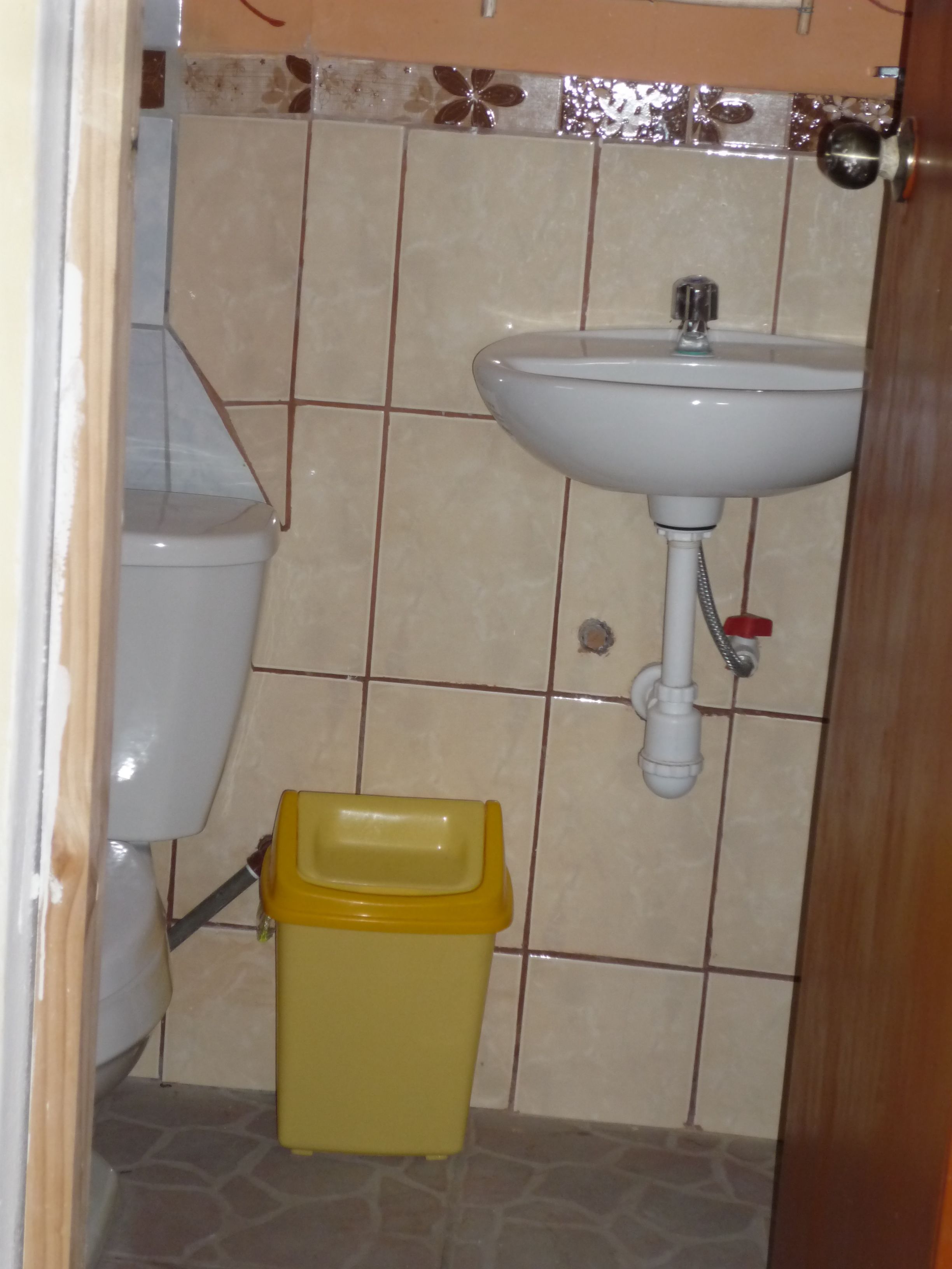 A bathroom with a toilet, sink, and yellow trash bin.