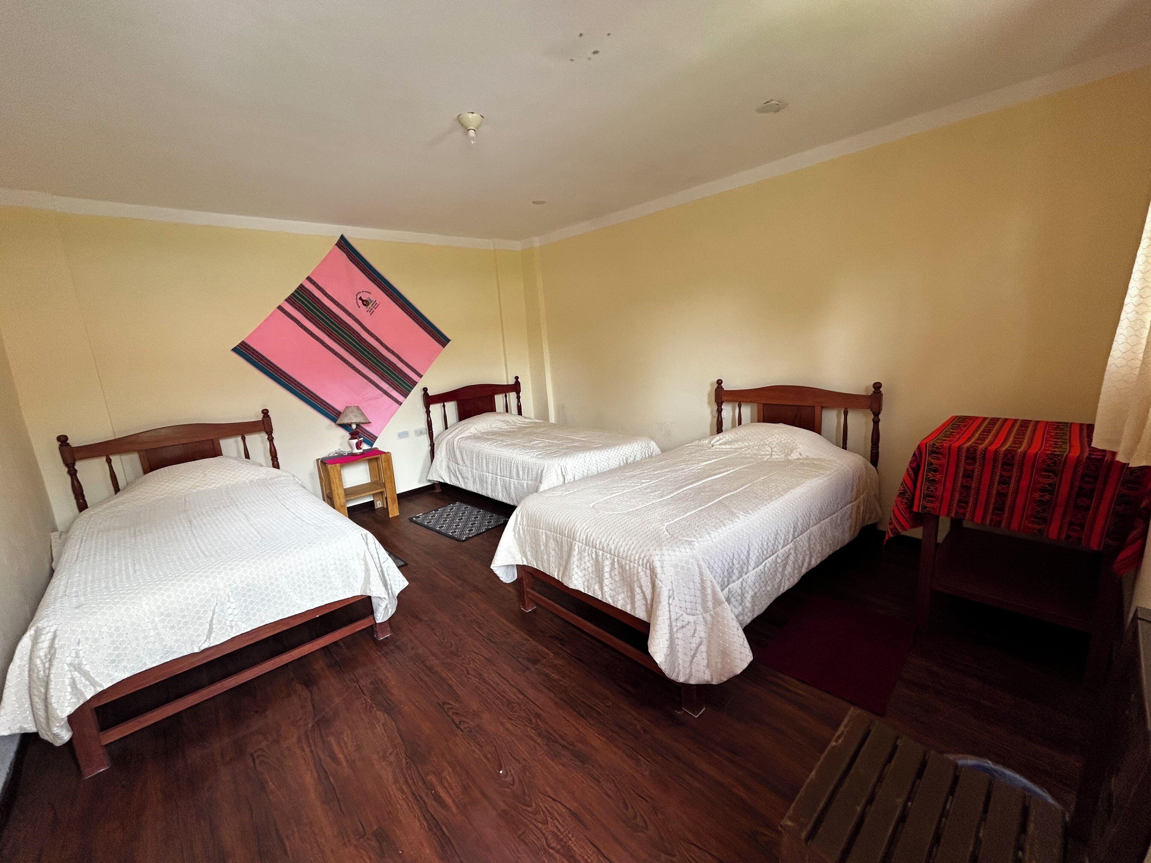A room with two wooden beds, a small table with a lamp, and a patterned wall hanging.