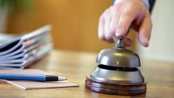 A hand ringing a bell on a wooden desk with a pen and papers.