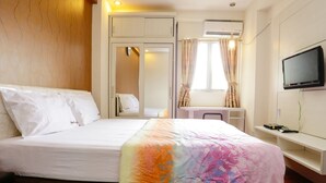 A hotel room with a bed, a vanity with a mirror, a television mounted on the wall, and an air conditioning unit. - RedLiving Apartemen The Suites Metro - Mary Tower E (Bandung)