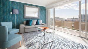 A modern living room with a teal accent wall, a large mirror, a grey sofa, a blue armchair, and a patterned rug. - Hillside Heights 503 by CTHA (Cape Town)