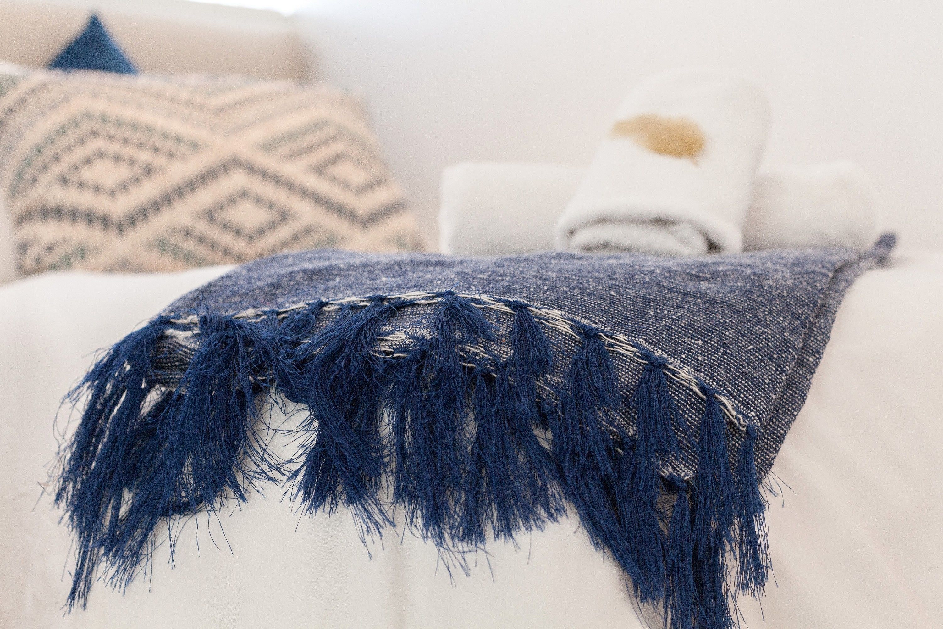 Ein Bett mit einer blauen Decke mit Fransen, einem weißen Kissen und einem gemusterten Kissen.