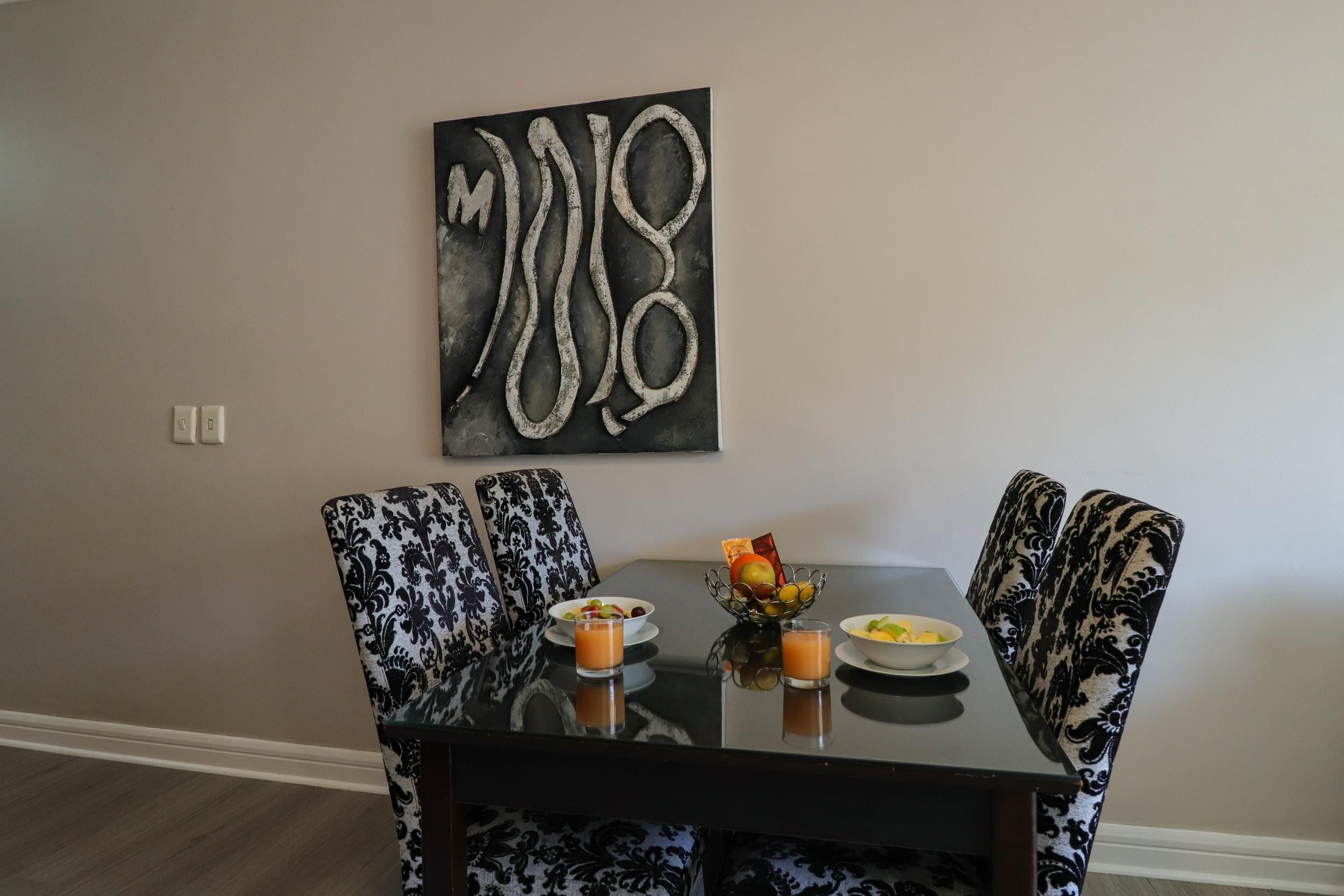 A dining area with a black table, patterned chairs, and a wall-mounted abstract art piece.