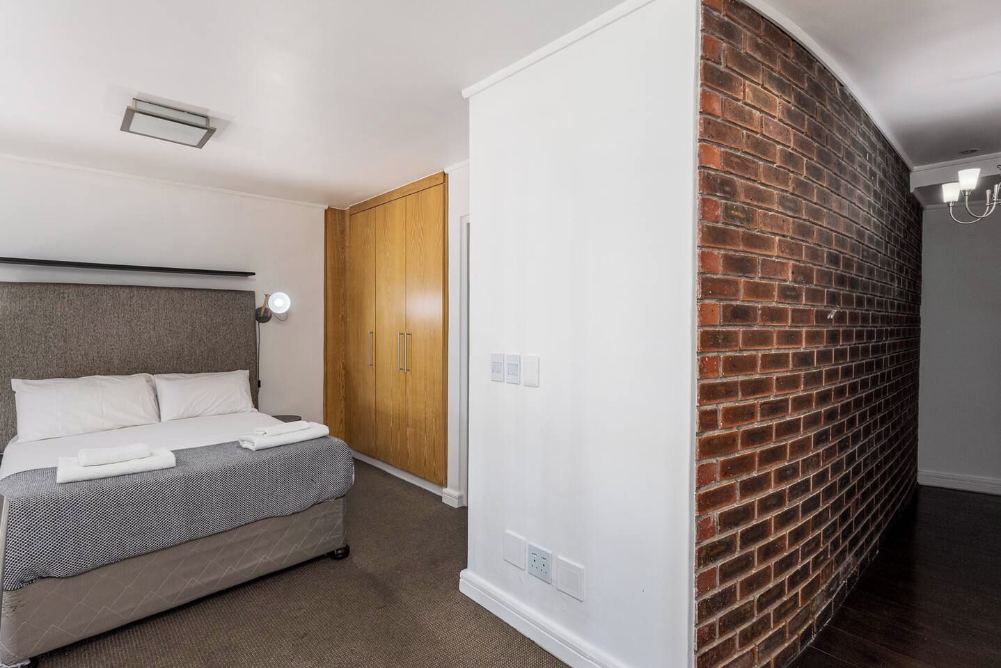 Une chambre à coucher avec un lit, une armoire, un mur en briques et un luminaire au plafond.