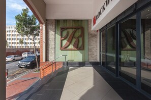 A building entrance with a large 'B' logo, a staircase, and a parking area with cars. - Rockwell Apartments by CTHA (Cape Town)