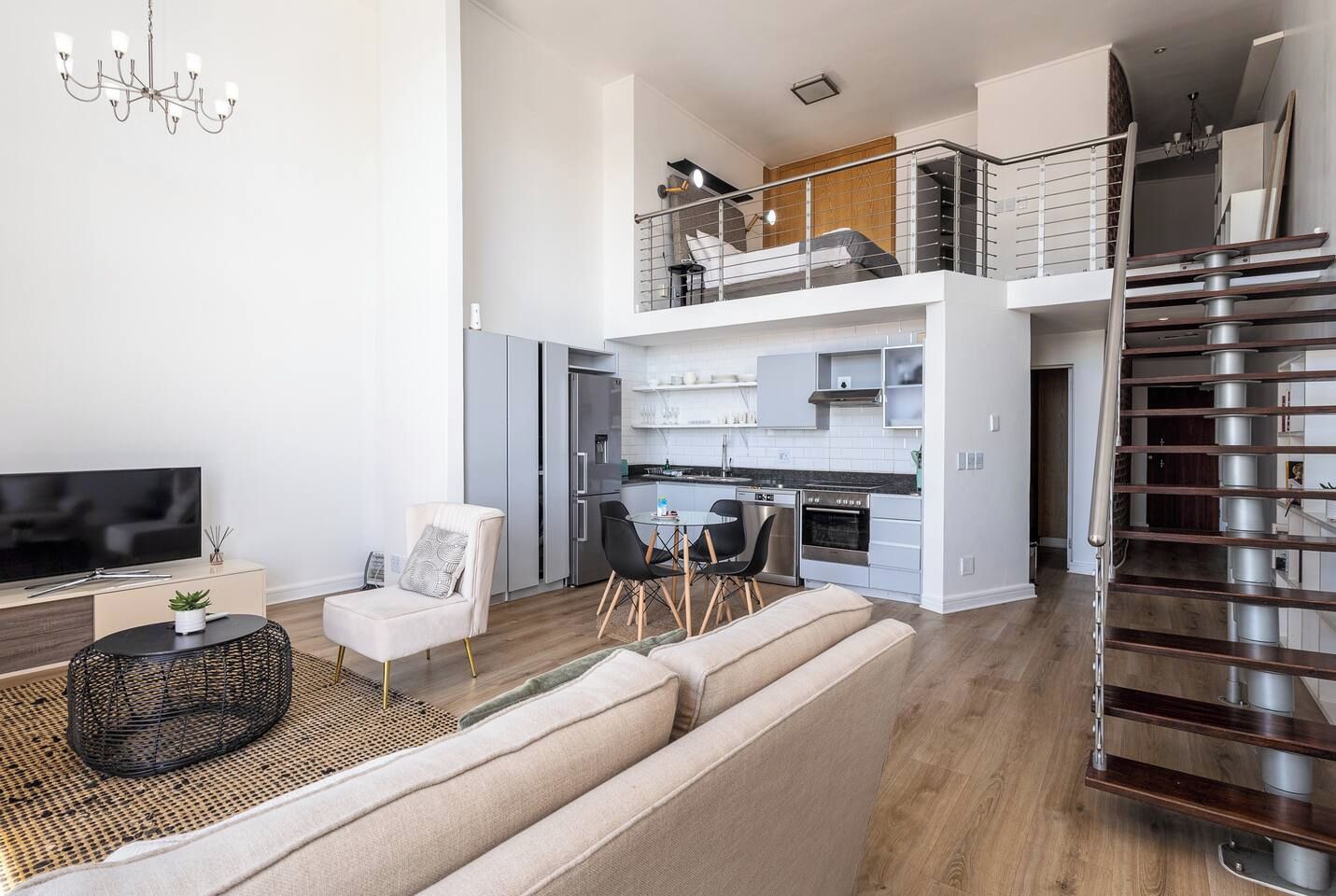 A modern apartment with a living room, kitchen, and a staircase leading to an upper floor.
