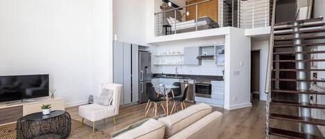 A modern apartment with a living room, kitchen, and a staircase leading to an upper floor.