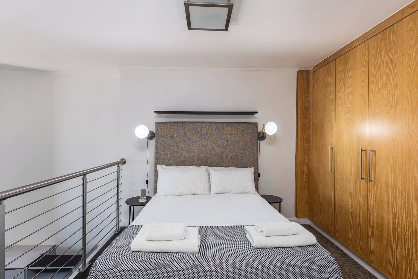 Una habitación de hotel con una cama, mesitas de noche, un armario y una barandilla.