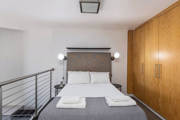 A hotel room with a bed, bedside tables, a wardrobe, and a railing.