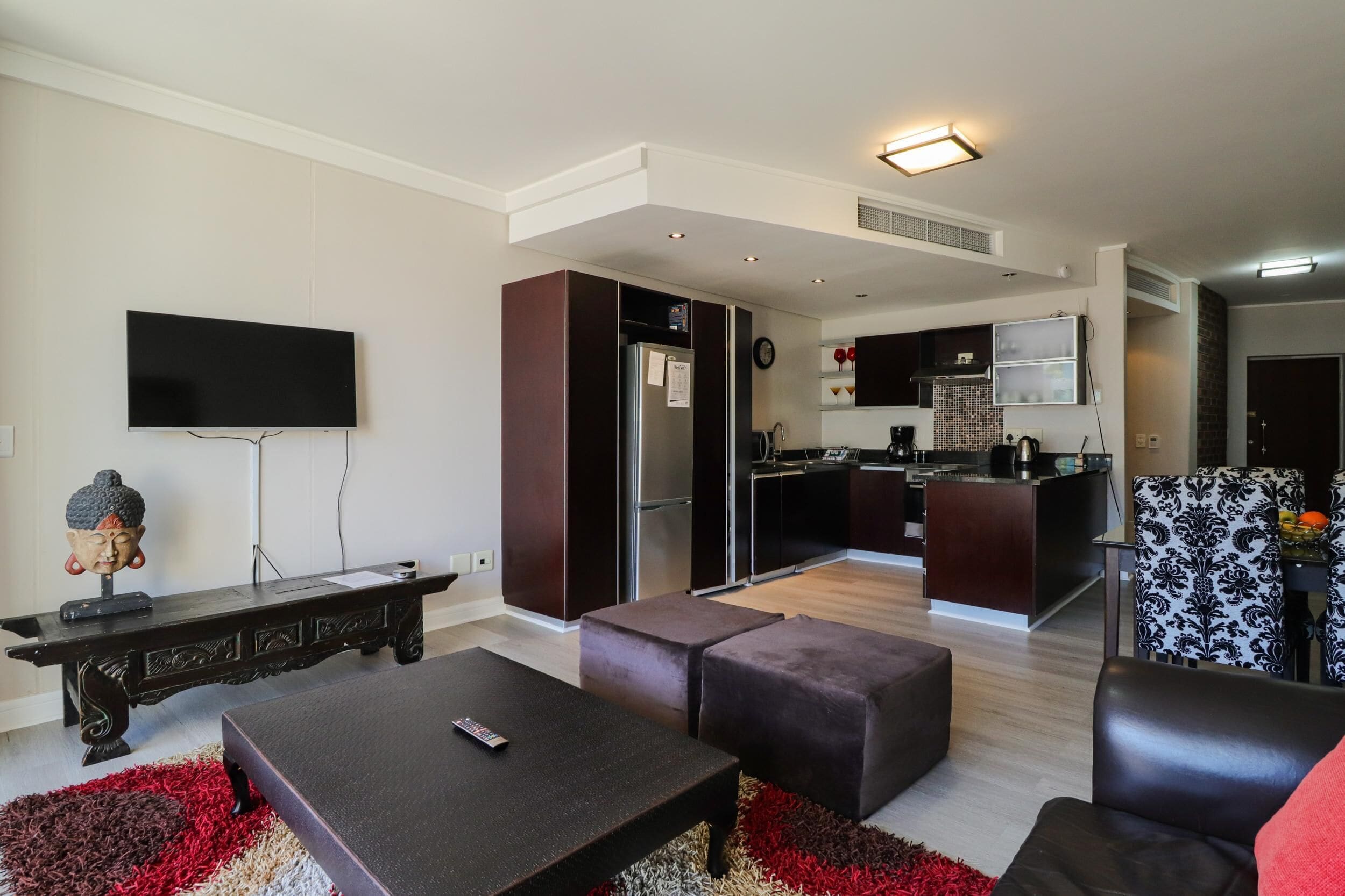 Un salon moderne avec un téléviseur à écran plat, une table basse de couleur sombre et un tapis rouge et beige.