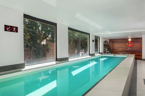 A long indoor swimming pool with clear glass walls, a wooden wall with a life preserver sign, and a tiled floor.