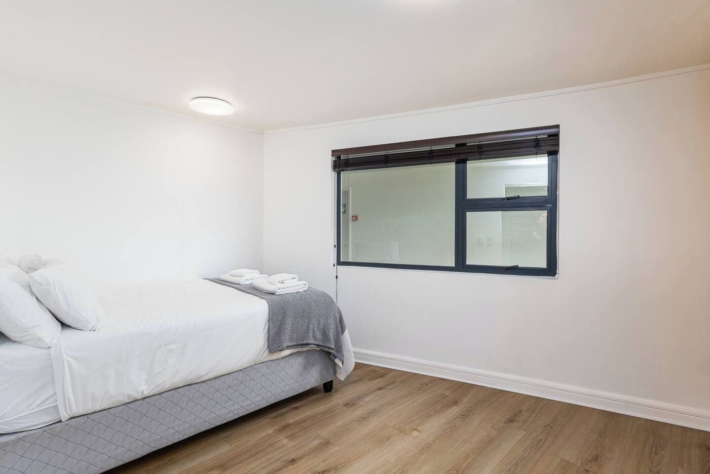 Un dormitorio con cama, una ventana con persianas, una mesita de noche y una lámpara fijada a la pared.