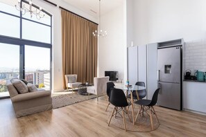 Un salon moderne comprenant un canapé, une table à manger avec des chaises, un téléviseur et une grande fenêtre avec des rideaux.